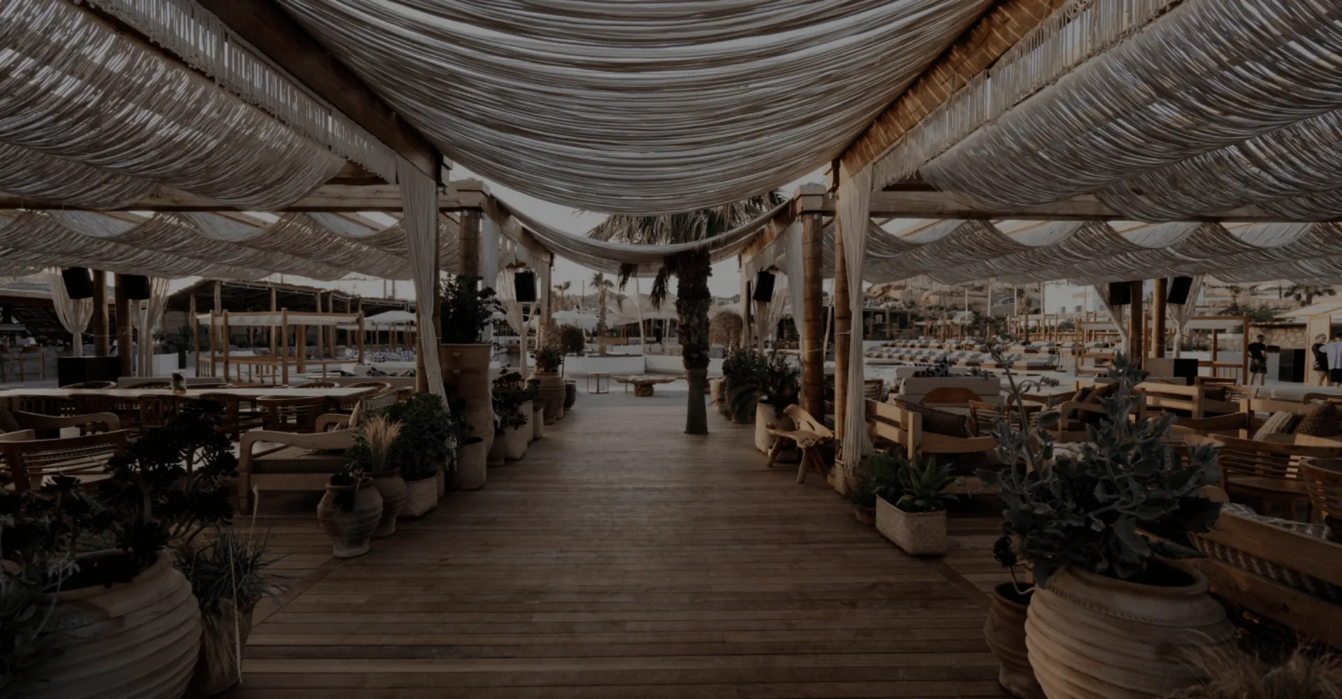 Covered walkway at SantAnna with draped fabric ceilings, wooden deck flooring, and Mediterranean potted plants.